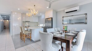 A modern kitchen with a dining area, featuring a chandelier, white cabinetry, and a large refrigerator. - The OC Home: Centrally Located, Home Away Home (Coconut Grove)