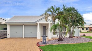 A residential property with two garage doors, a landscaped front yard with palm trees, and a brick driveway. - The OC Home: Centrally Located, Home Away Home (Coconut Grove)