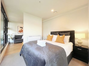 A modern bedroom with a large bed, a nightstand, a side table, and a sofa. - Comfy 1-bedroom Studio in Auckland CBD (Auckland)