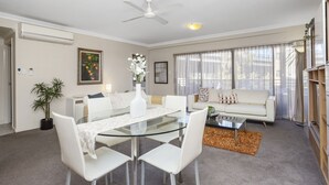 A modern living room with a glass dining table, white sofas, and a ceiling fan. - Prime 2BR Suite on Mounts Bay Road (Perth)