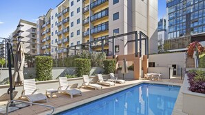 A swimming pool with lounge chairs and a sun terrace, surrounded by modern buildings. - Prime 2BR Suite on Mounts Bay Road (Perth)