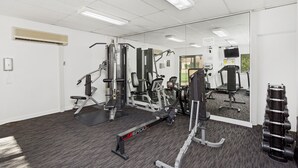 Ett gym med olika typer av träningsredskap, en spegel och en TV som är monterad på väggen.