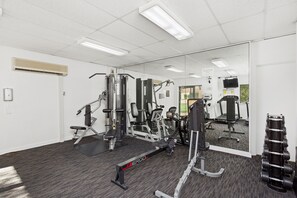 A gym with various exercise equipment, a mirror, and a wall-mounted TV. - Prime 2BR Suite on Mounts Bay Road (Perth)