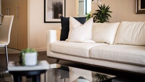 A modern living room with a white leather sofa, a black and white pillow, a small potted plant, and a glass coffee table. - Prime 2BR Suite on Mounts Bay Road (Perth)