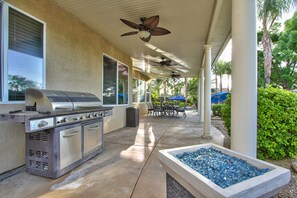 Un patio exterior con una parrilla empotrada, un ventilador de techo y una chimenea.