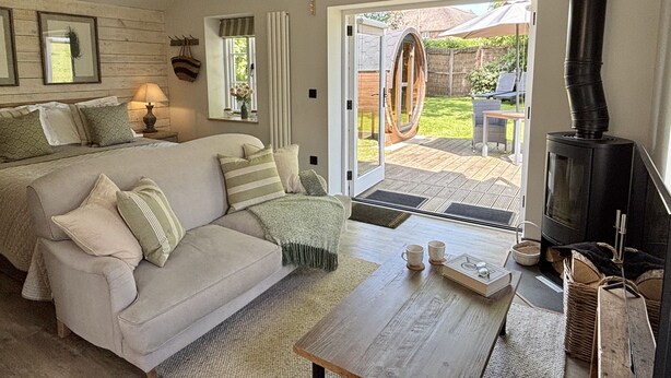 A cozy bedroom with a bed, a sofa, a table with mugs, a fireplace, and a view of the outdoors. - Drovers Run - Beaminster, Dorset (Chard)