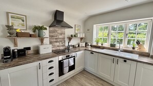 A kitchen with white cabinets, a wooden countertop, a stove, and a window with a view of greenery. - Drovers Run - Beaminster, Dorset (Chard)