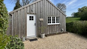 A wooden shed with a white door and window, surrounded by gravel and greenery. - Drovers Run - Beaminster, Dorset (Chard)
