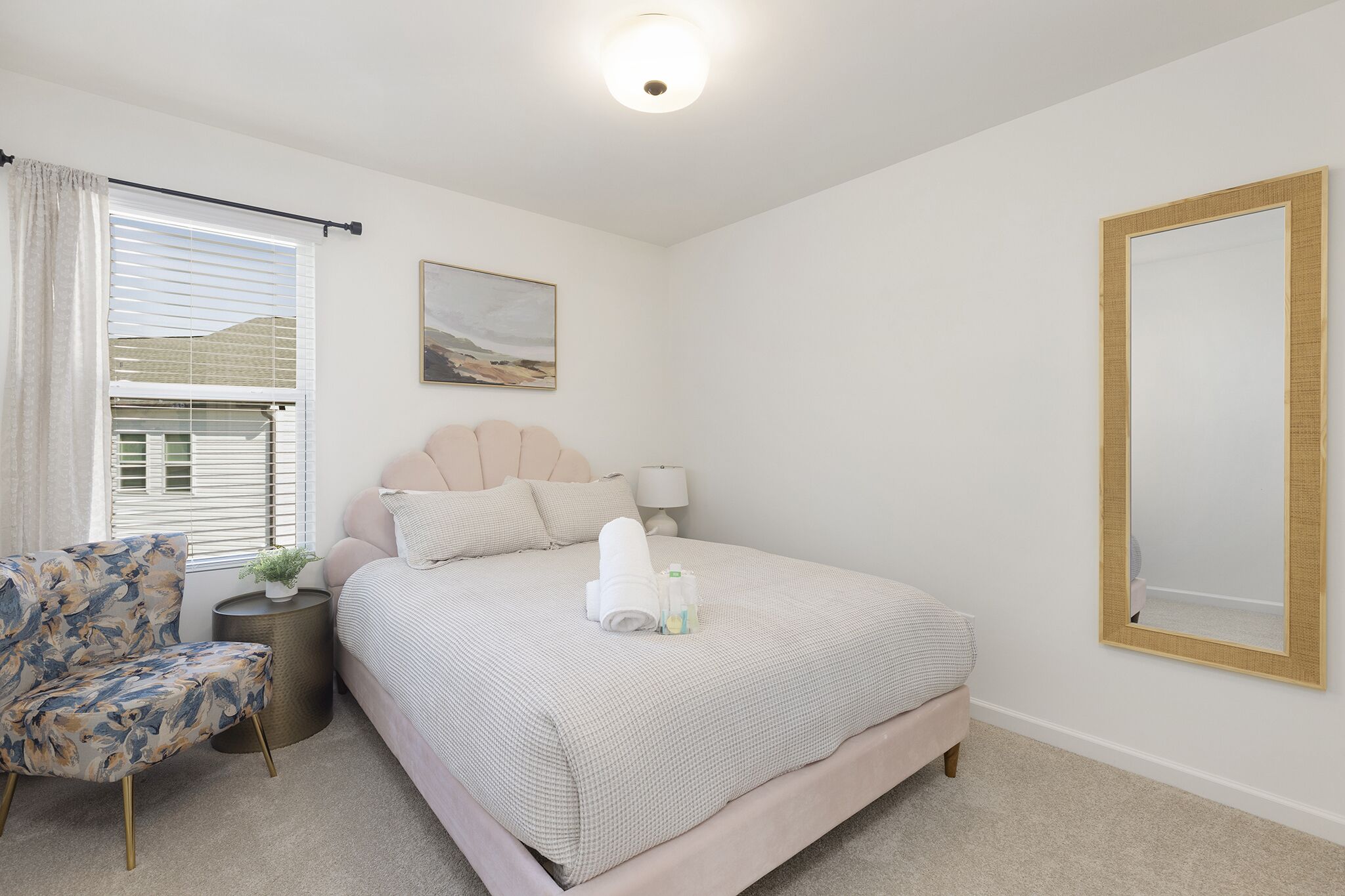 A neatly arranged bedroom with a bed, a chair, a bedside table, and a wall-mounted mirror.