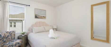 A neatly arranged bedroom with a bed, a chair, a bedside table, and a wall-mounted mirror.