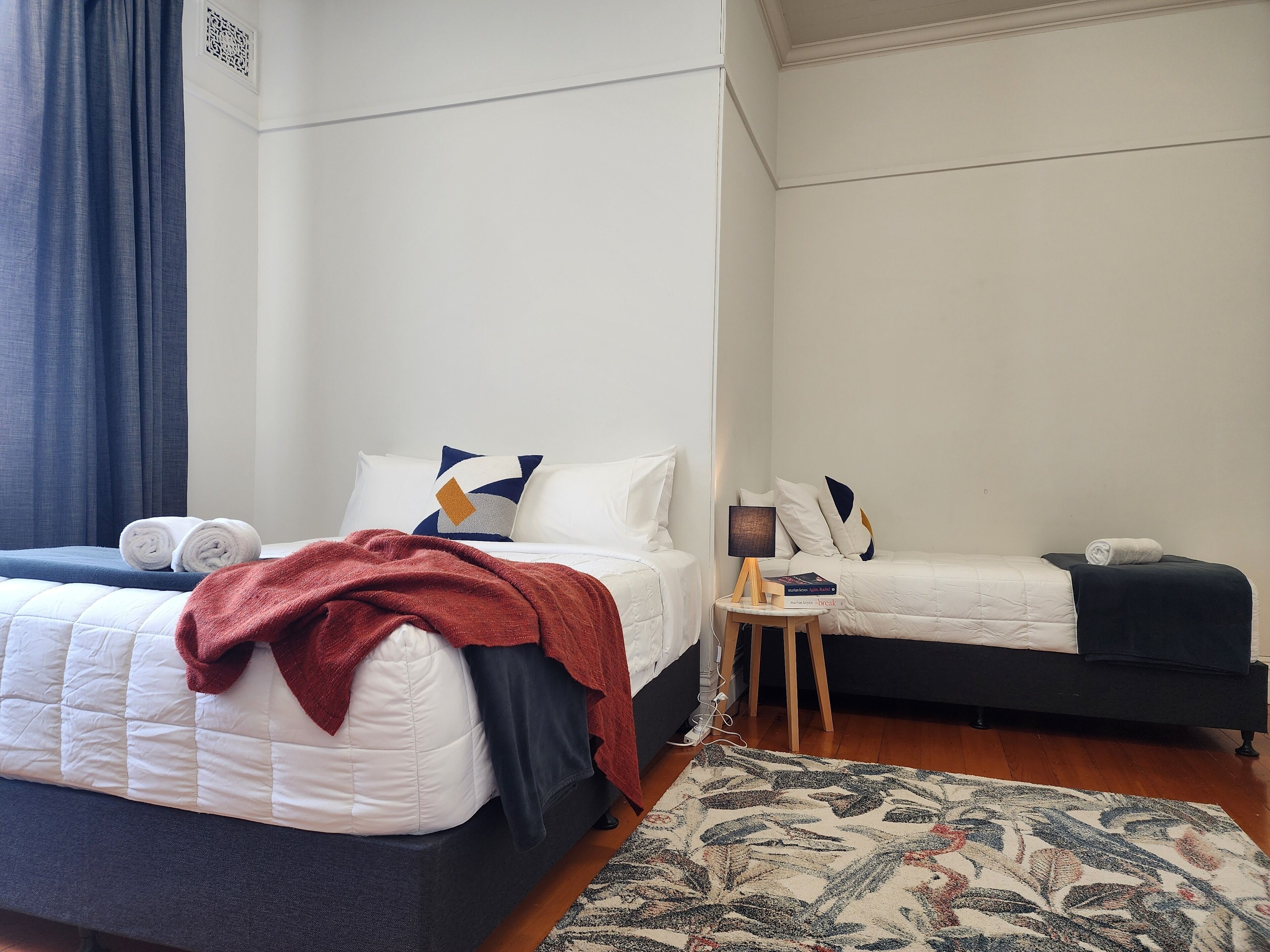 A hotel room with two beds, a small table with a lamp, and a patterned rug.
