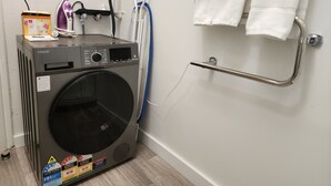 A laundry area with a front-loading washing machine, an iron, and a drying rack. - U Suites on Cuba (Wellington)