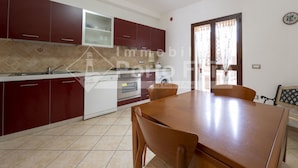 Uma cozinha moderna com armários vermelhos, bancada branca e área de refeições com mesa e cadeiras de madeira.