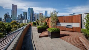 Una terraza en la azotea con vistas a la ciudad, suelo de madera y macetas con plantas.
