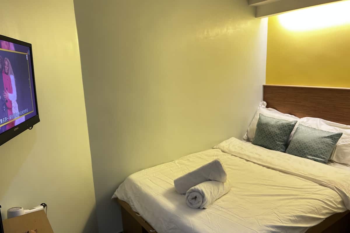 A hotel room with a bed, pillows, a TV mounted on the wall, and a small table with a remote control.
