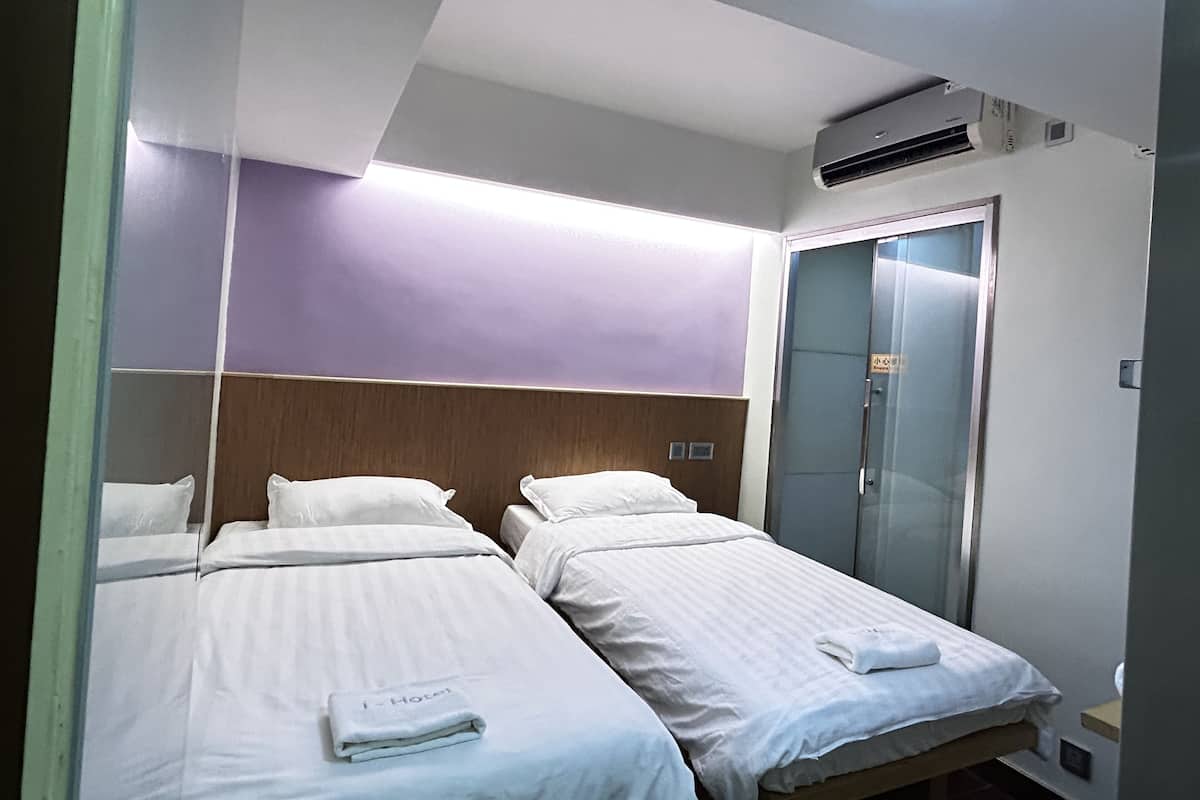 A hotel room with two beds, a wardrobe, and an air conditioning unit.