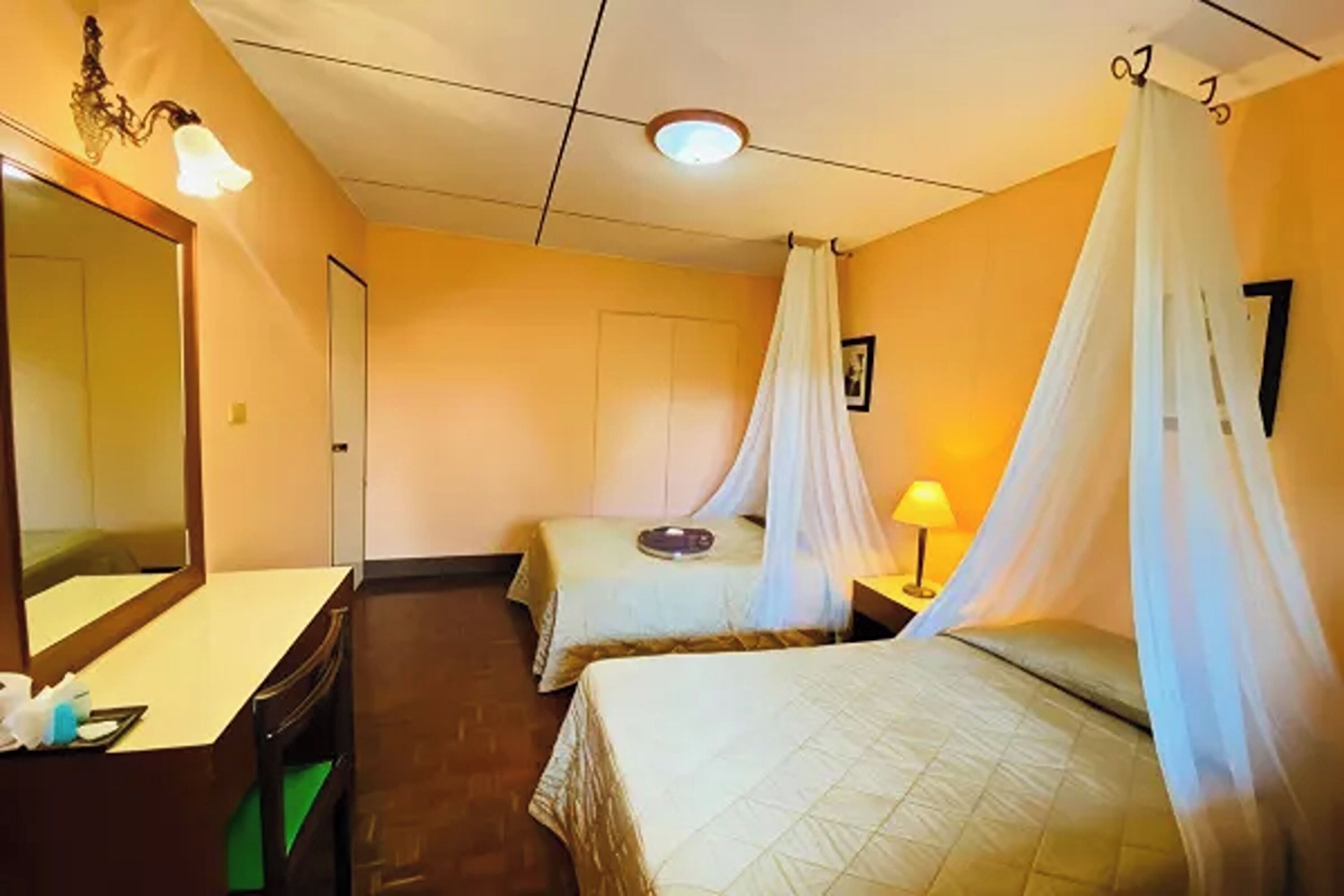 A hotel room with two beds, a large mirror, a bedside table, a lamp, and a door.