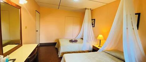 A hotel room with two beds, a large mirror, a bedside table, a lamp, and a door.