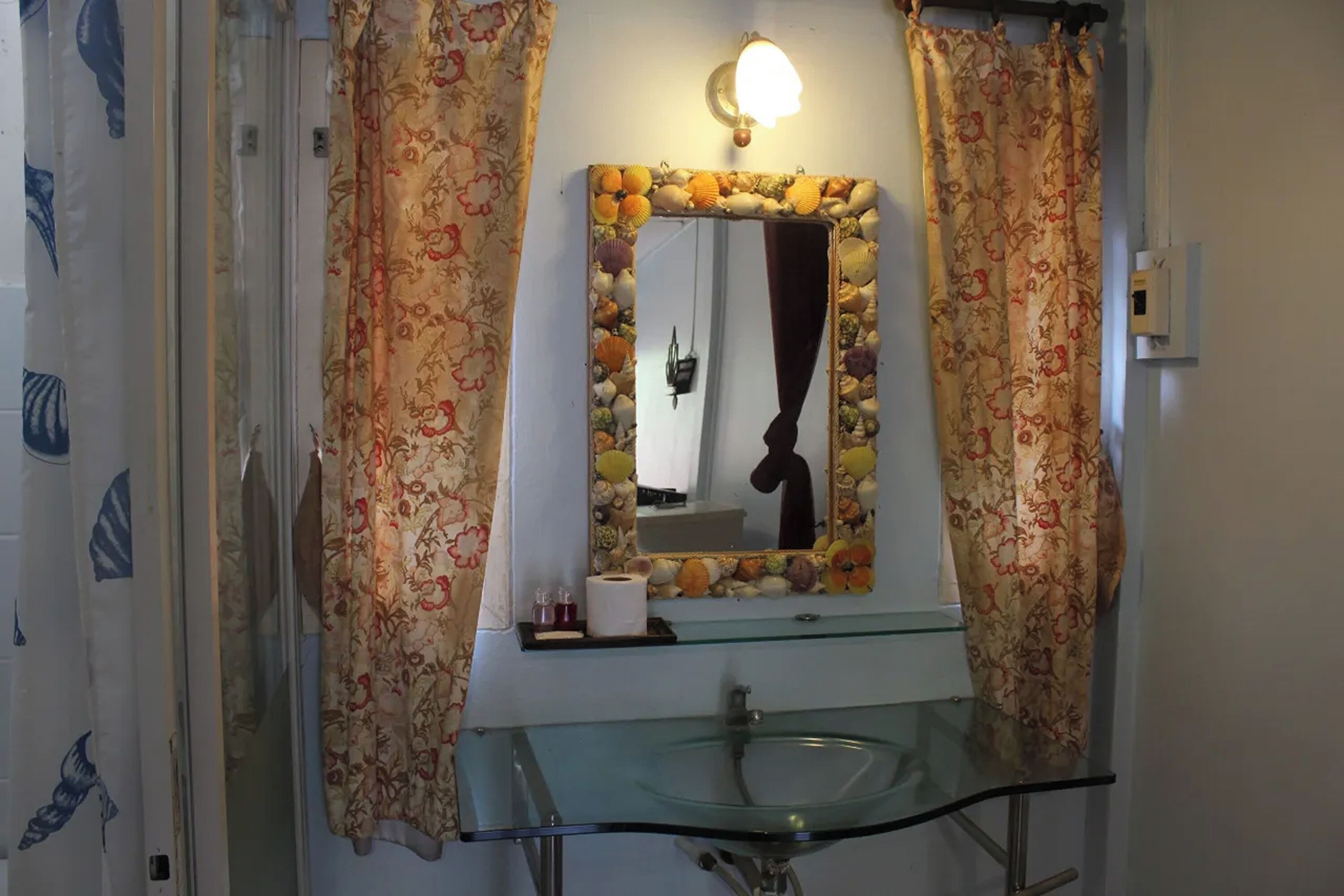 A bathroom with a glass sink, a mirror with a decorative frame, and floral curtains.