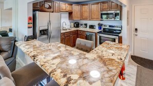 A kitchen with granite countertops, wooden cabinets, a refrigerator, microwave, stove, and dishwasher.