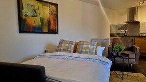 A modern bedroom with a large bed, a small table with a plant, a sofa, and a kitchen in the background. - Spacious London Apartment, 5mins from metro (London)