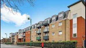 A row of modern apartment buildings with balconies, a clear sky, and a street with a red mailbox. - Spacious London Apartment, 5mins from metro (London)