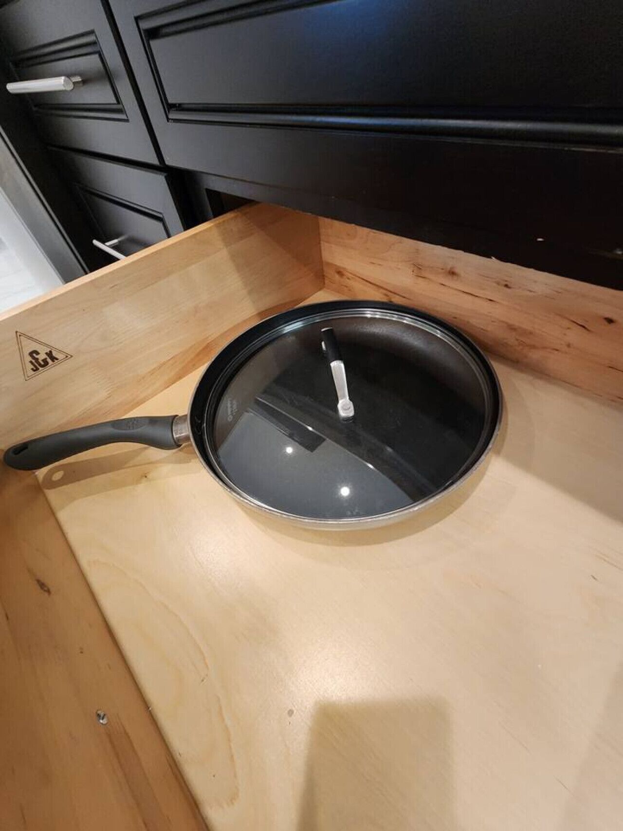 A black frying pan with a lid on a wooden countertop.