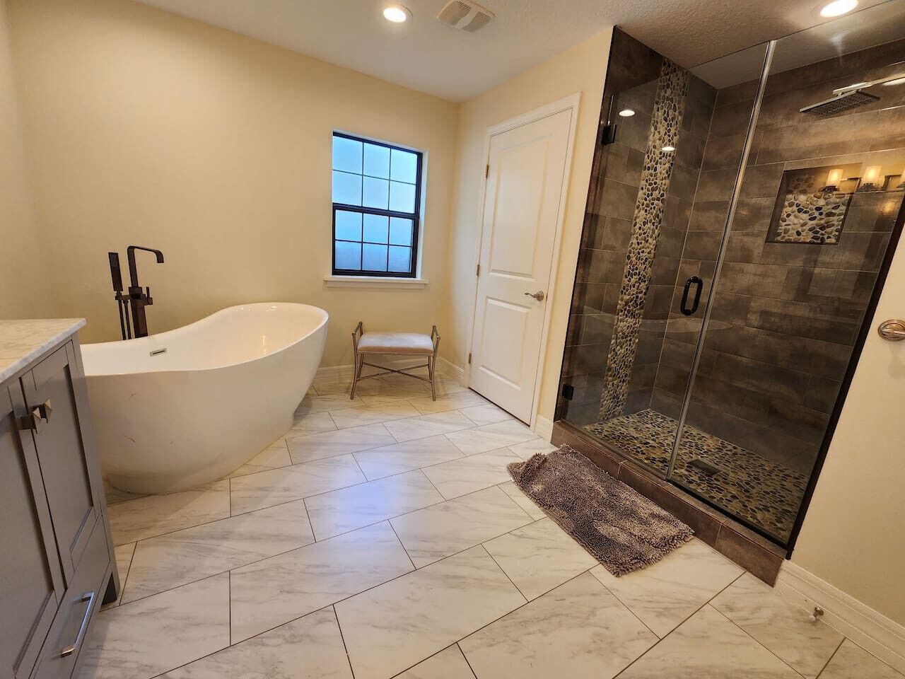 Un bagno con una vasca freestanding, una doccia con parete in pietra e una piccola finestra.