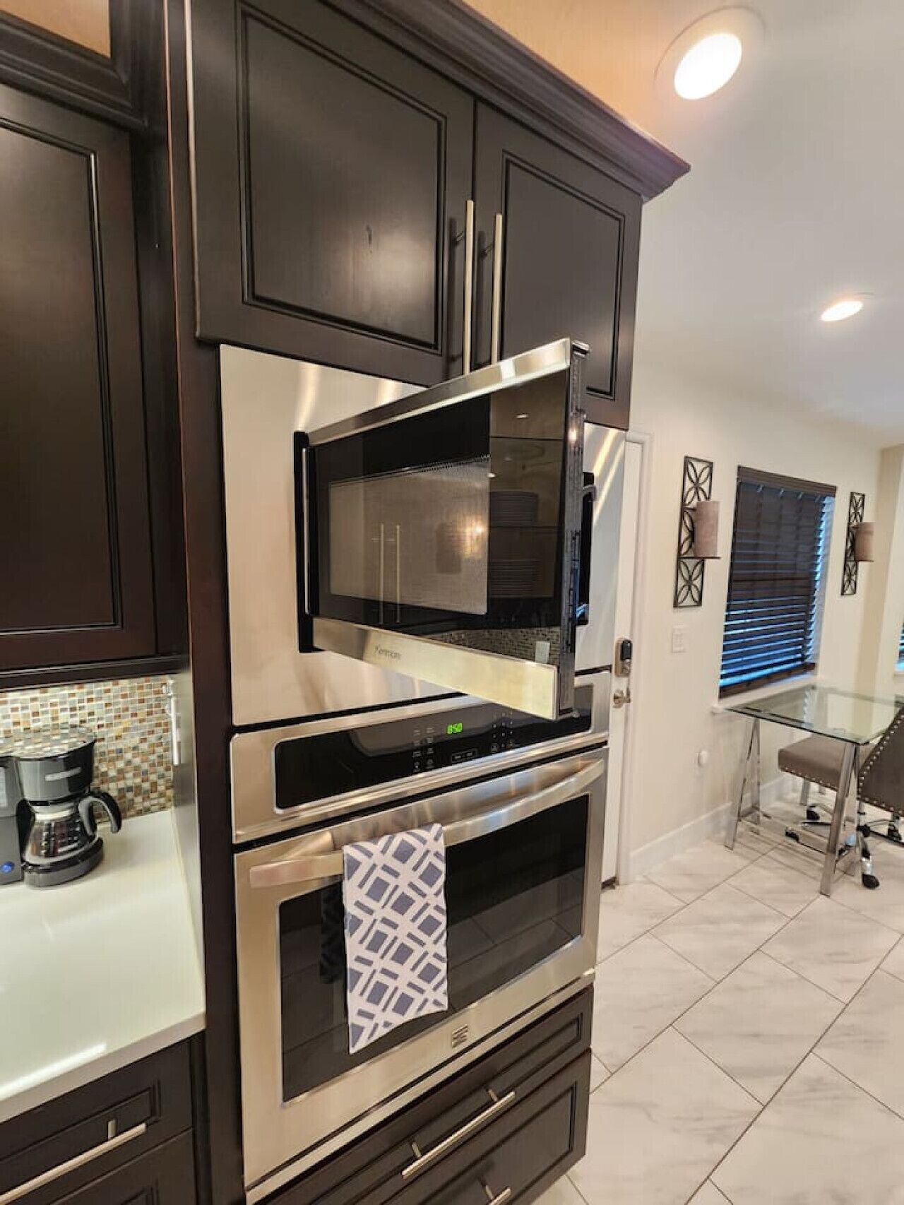 A modern kitchen with dark cabinetry, stainless steel appliances, and a glass dining table.