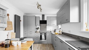 A modern kitchen with grey cabinets, a wooden dining table, and a built-in oven. - Swan's Nest - River view, Close to beach, Garden (Torcross)