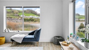 A bedroom with a large window offering a view of a lake and houses. - Swan's Nest - River view, Close to beach, Garden (Torcross)