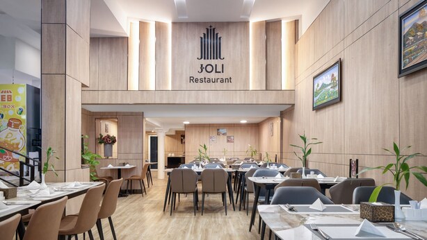 A JOLI Restaurant with a modern interior, featuring wooden panel walls, multiple dining tables with chairs, and framed artwork on the walls. - Joli Hotel (Phnom Penh)