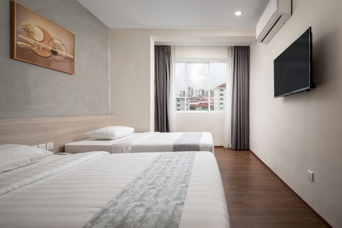 A hotel room with two beds, a large window with curtains, a mounted TV, and a painting on the wall.