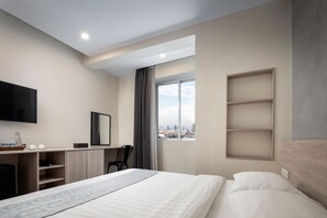 A modern hotel room with a bed, a desk, a TV, and a window with a city view. - Joli Hotel (Phnom Penh)