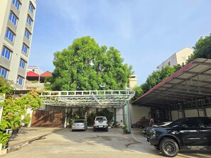 A parking area with a covered walkway, two cars, and a black SUV. - Joli Hotel (Phnom Penh)