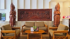 A lobby with two wooden chairs, a sofa, a coffee table, and two large wooden statues. - Joli Hotel (Phnom Penh)