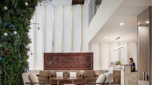 A lobby with a reception desk, a large wall tapestry, and a seating area with sofas and chairs. - Joli Hotel (Phnom Penh)