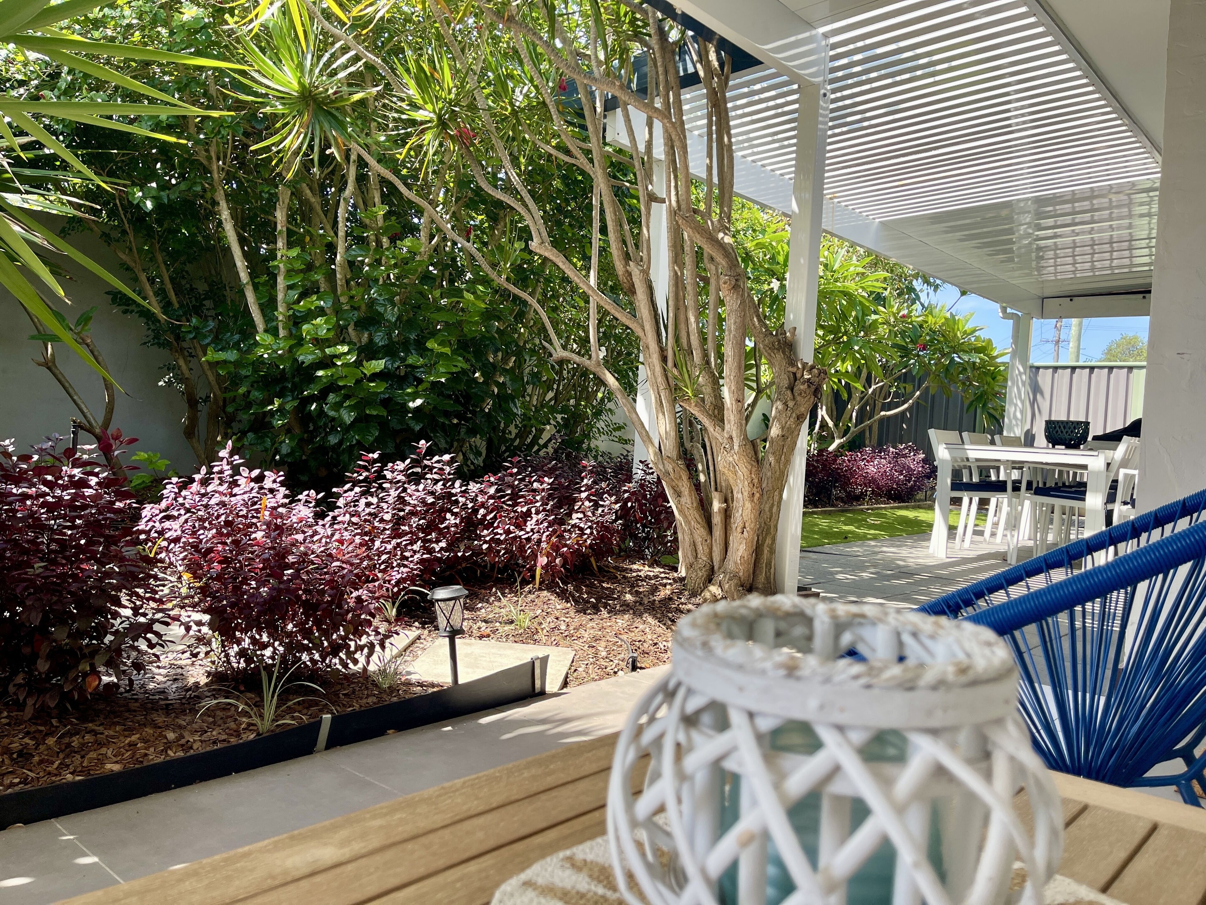 Un patio techado con una mesa y sillas blancas, rodeado de abundante vegetación y una hamaca.