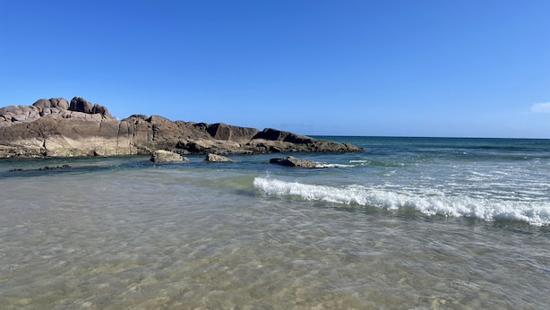 Een strand met helder water, rotsformaties en een heldere lucht.