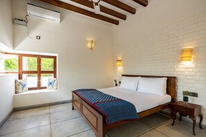 A bedroom with a wooden bed, white brick wall, two wall sconces, a window with a view, and an air conditioning unit. - Amã Stays & Trails Forest Home, Hosur (Hosur)