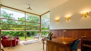 A spacious room with large windows, a wooden dining table, and a red sofa.