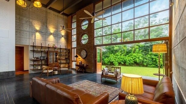 A spacious living area with a large window, leather sofas, a coffee table, and a bookshelf.