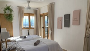 A bedroom with two beds, a ceiling fan, a window with curtains, and wall art.
