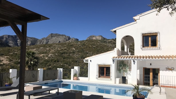A two-story house with a swimming pool, outdoor seating, and a view of mountains.