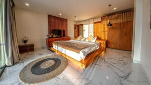 A spacious bedroom with a large bed, wooden headboard, and a marble floor. There is a wooden wardrobe and a television on a wooden stand.