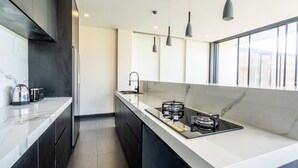 A modern kitchen with dark cabinetry, a white marble countertop, a gas stove, and pendant lighting.