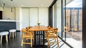 A modern dining area with a wooden table and chairs, a vase of flowers, and a view through large windows.