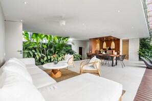 A modern living room with a white sofa, a round coffee table, and a dining area with a wooden table and wicker chairs.