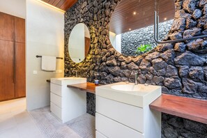 A bathroom with two sinks, a wooden vanity, a large mirror, and a stone wall.