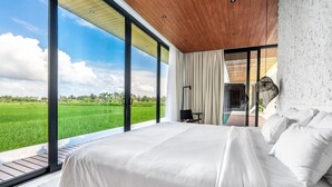 A bedroom with a large bed, a view of a green field, and a wooden ceiling. - Amazing 3BR Green Flow Villa in Ubud with Pool (Kec. Ubud)